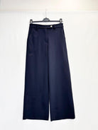 A pair of dark navy blue trousers hanging on a black hanger against a plain white background.