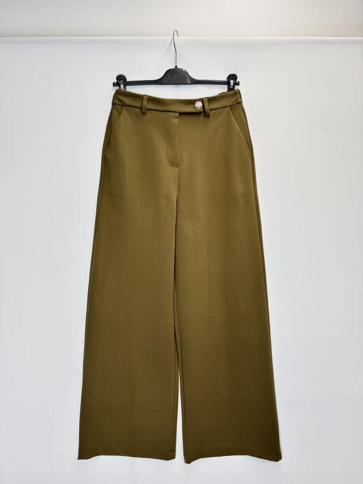 A pair of olive green wide-leg cropped pants hanging on a black hanger against a plain white wall.
