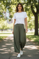 Woman wearing a white t-shirt and green wide-leg pants walking on a path with trees in the background.