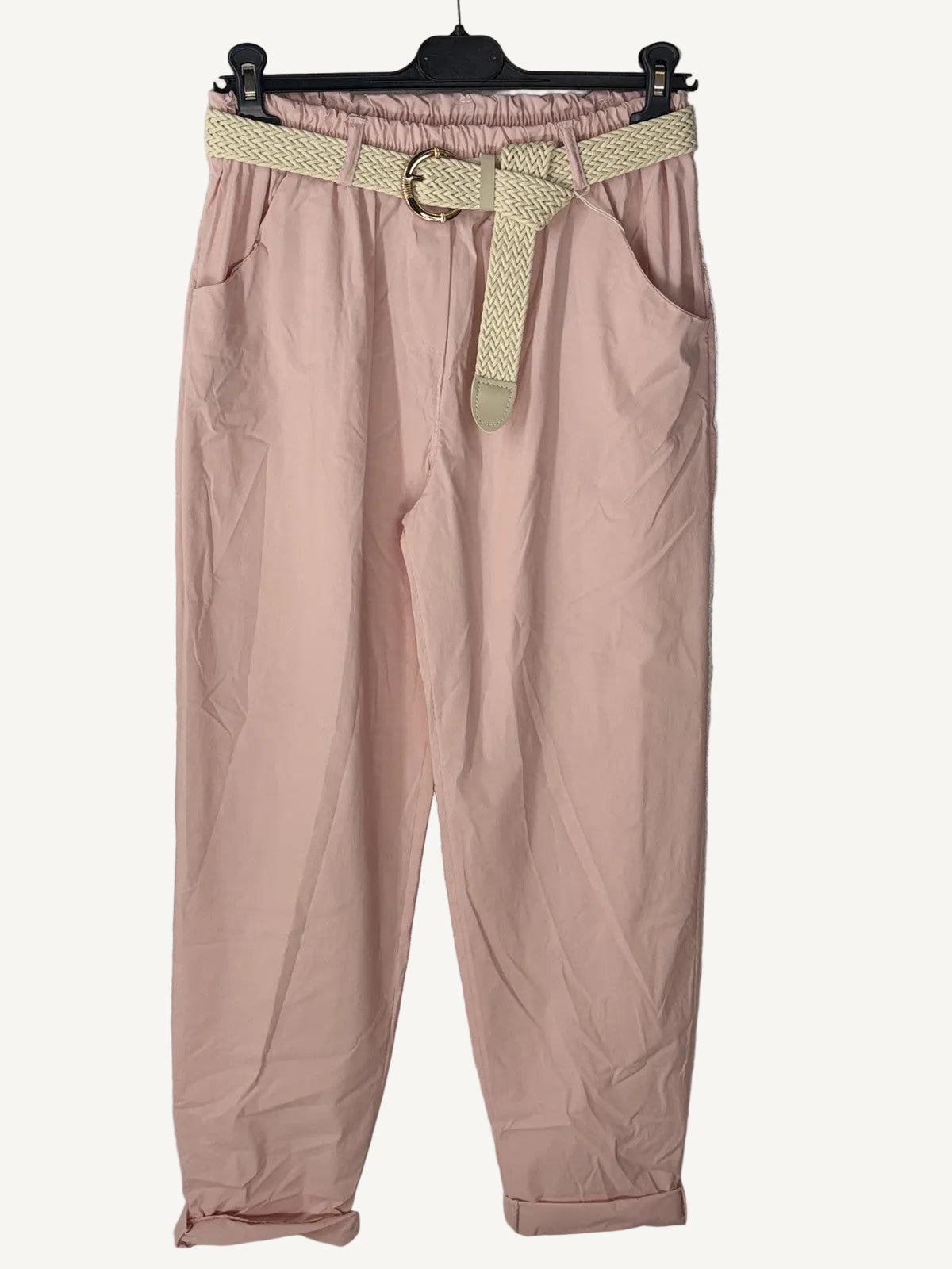 Pink pants with a belt on a hanger against a textured wall.