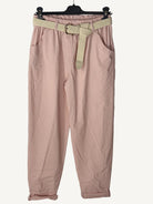 Pink pants with a belt on a hanger against a textured wall.