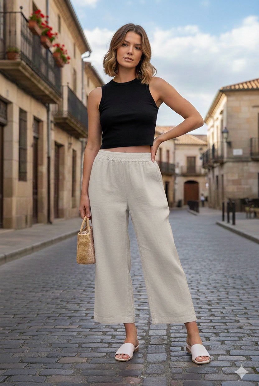Woman in black top and beige pants standing on a street with buildings in the background
