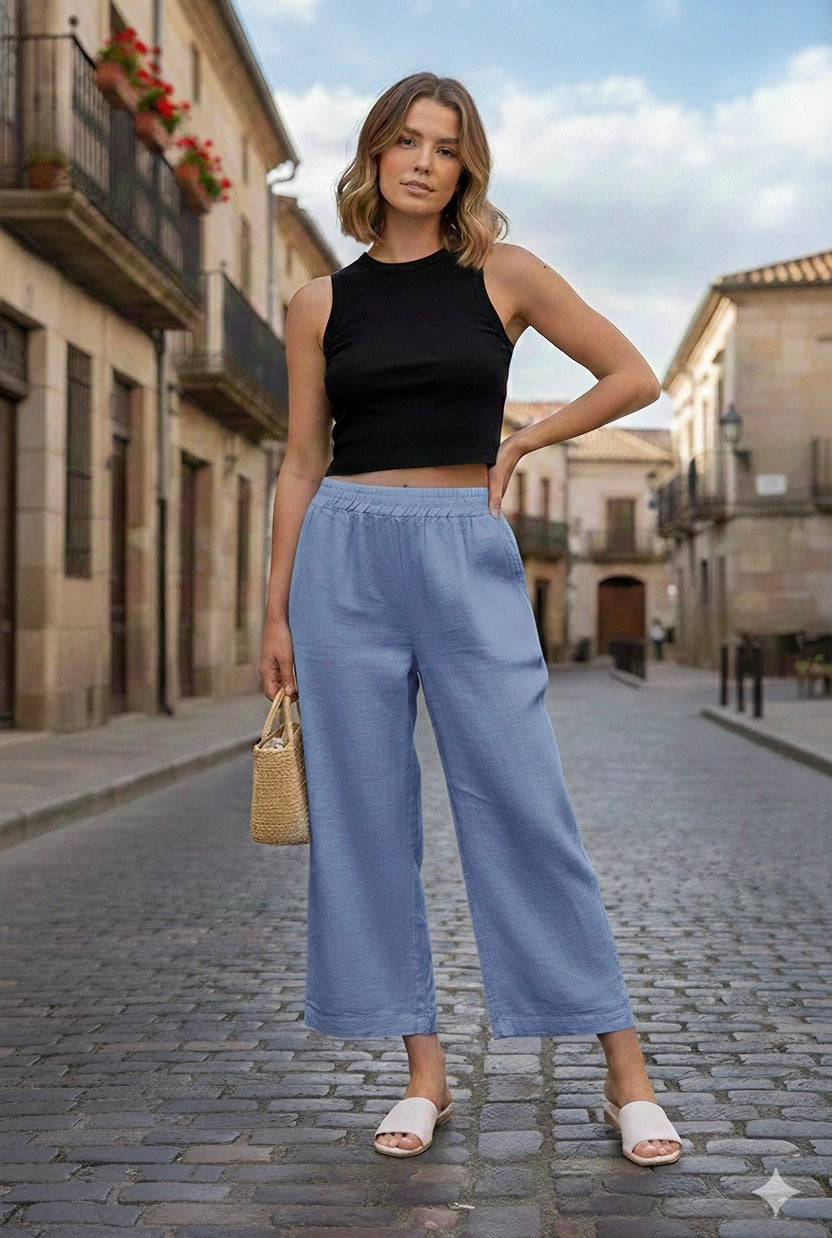 Woman in black top and blue pants standing on a cobblestone street.