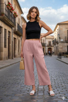 Woman in black top and pink pants standing on a street with buildings in the background