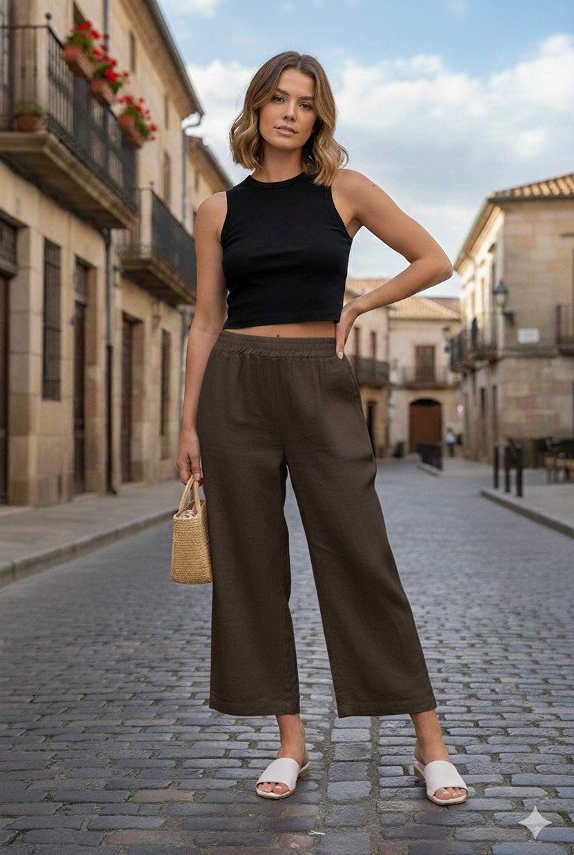 Woman in black top and brown pants standing on a street with buildings in the background