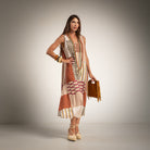A woman models a sleeveless, round neck maxi dress with a patchwork print in beige, brown, and orange tones