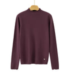 A long-sleeve knit sweater in deep plum purple, hanging on a wooden hanger against a plain white background. The sweater features a mock neck with delicate ruffled trim, matching ruffled trim along the cuffs, and a small white embroidered heart on the lower left hem.