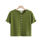 An olive green short-sleeve knit cardigan sweater hanging on a wooden hanger against a white background, featuring a black button placket with buttons and a small heart detail near the lower right hem.