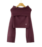 A dark plum purple knit long-sleeve top with a draped, layered cowl neck design, hanging on a wooden hanger against a plain white background. A small white heart detail is visible on the lower right of the front panel.
