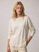 A blonde woman wearing a cream-colored crewneck sweater with front patch pockets and matching light beige trousers