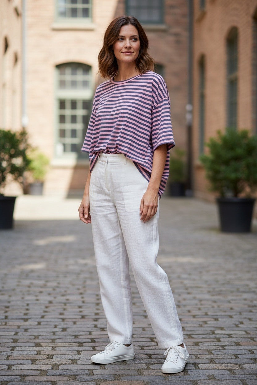 Woman wearing a striped shirt and white pants standing on a cobblestone street.