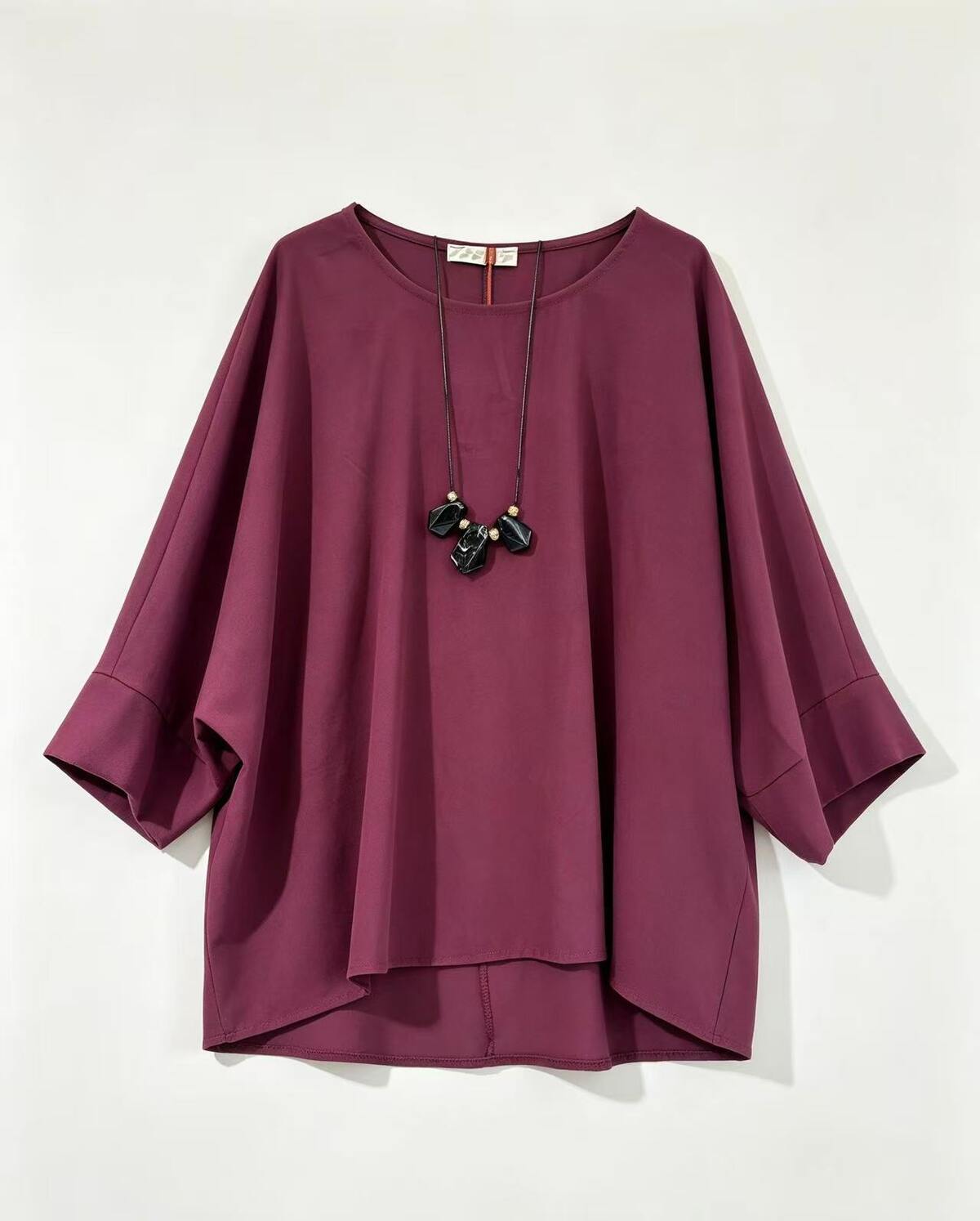 A loose-fitting, round neck top in burgundy, styled with a black pendant necklace
