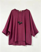 A loose-fitting, round neck top in burgundy, styled with a black pendant necklace