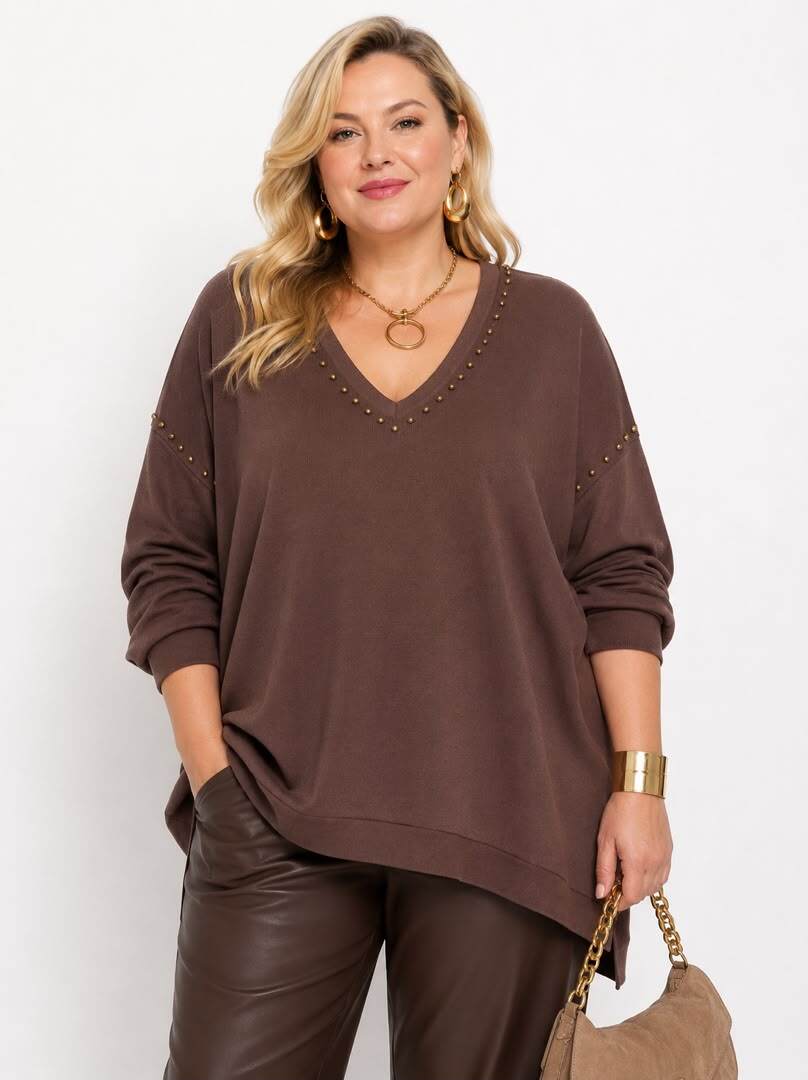 A woman modeling a brown long-sleeve V-neck top with small metallic stud embellishments along the neckline and sleeve edges, paired with brown pants against a plain light background.