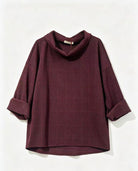 A dark burgundy cowl-neck top with a subtle grid pattern and rolled-up sleeves, displayed against a plain off-white background.