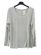 An ivory long-sleeve scoop neck top hanging on a black hanger against a textured light gray wall.