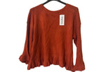 A rust-orange knit sweater with long sleeves and a ruffled hem,