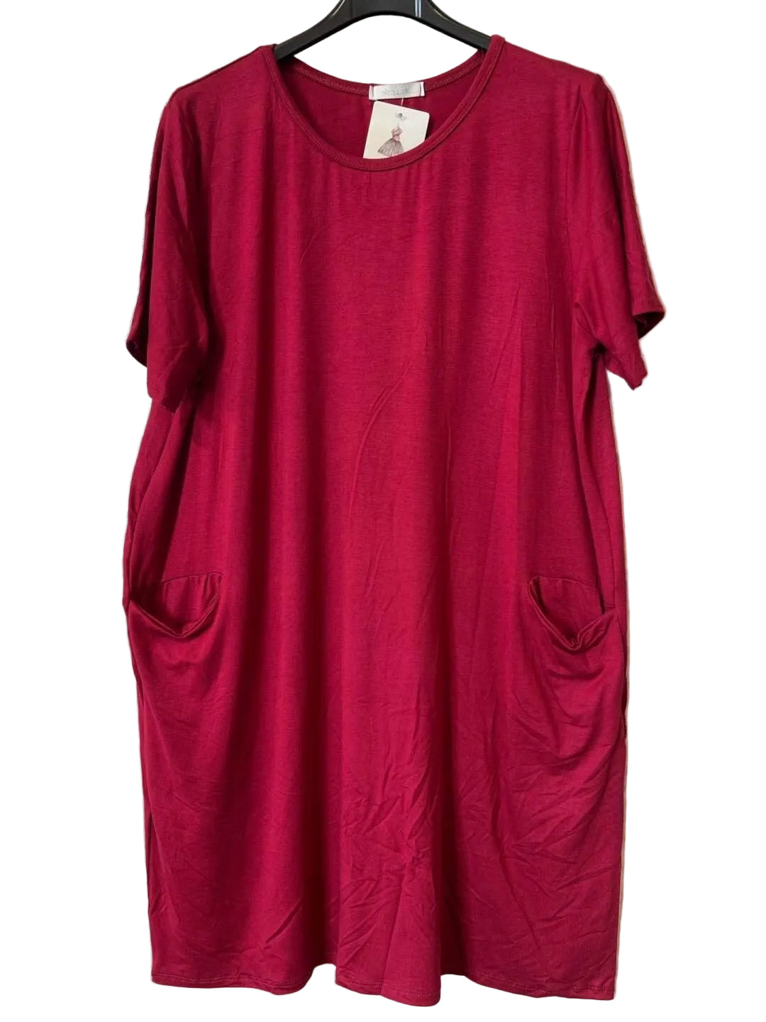 A short-sleeve crewneck dress in a burgundy colour, hanging on a black hanger against a textured gray wall. The dress features side pockets and a small white brand tag at the neckline.
