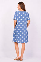 Woman wearing a blue dress with white polka dots on a plain background
