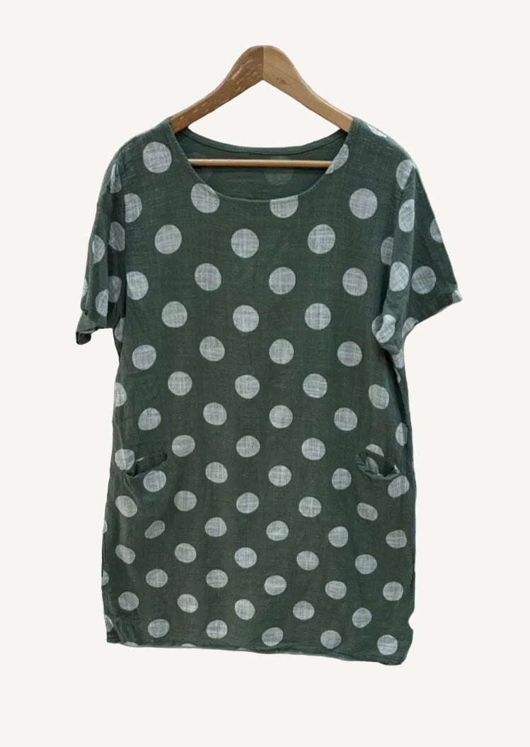 Green dress with white polka dots on a wooden hanger against a white background