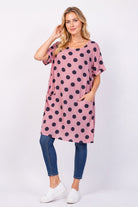 Woman wearing a pink polka dot dress with blue jeans on a white background