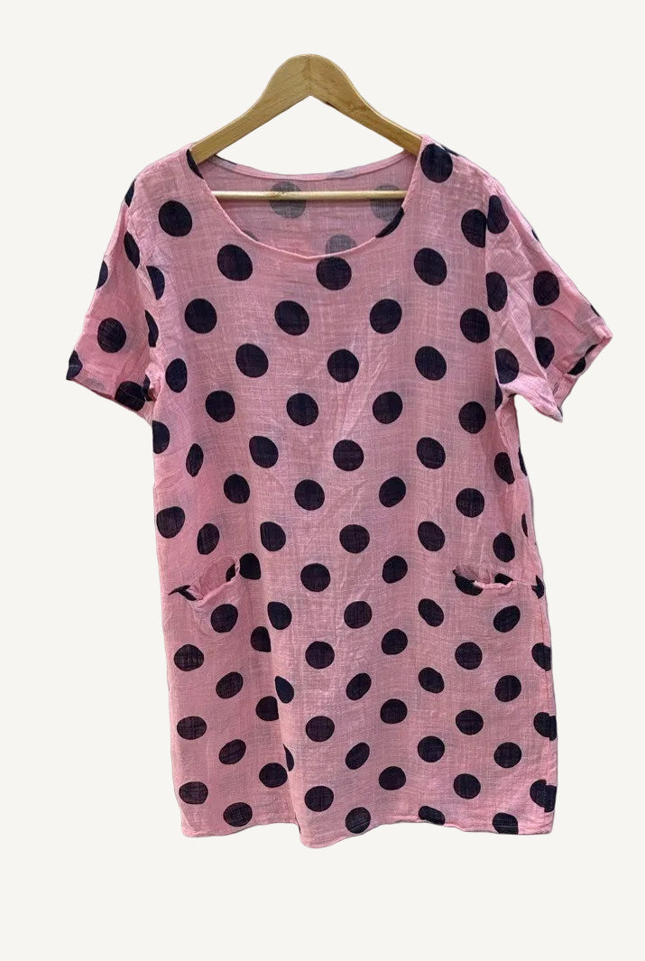 Pink dress with black polka dots on a hanger against a white background