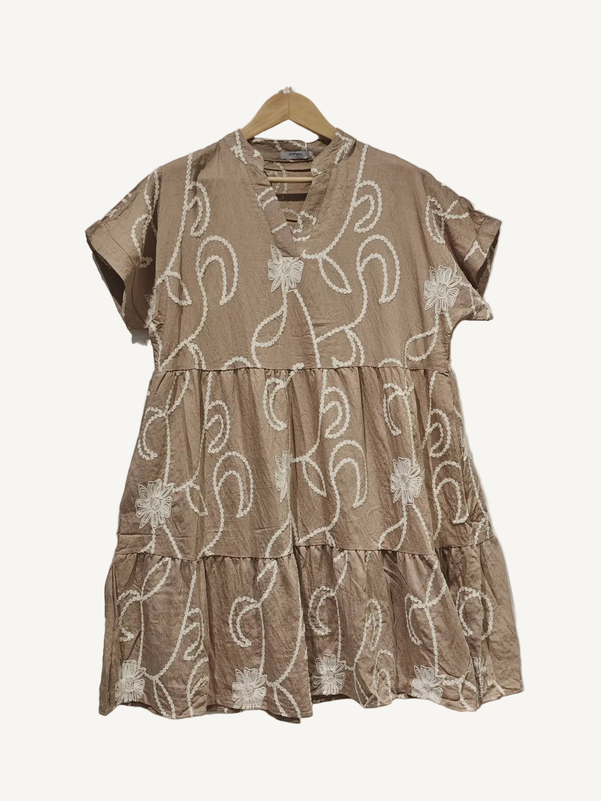 Beige dress with white floral embroidery on a hanger against a plain background