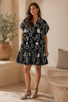 Woman wearing a black dress with white floral patterns in an indoor setting.