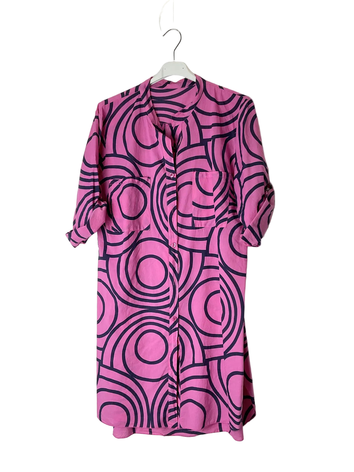 A pink and black geometric patterned shirt dress hanging on a white plastic hanger against a plain white wall.