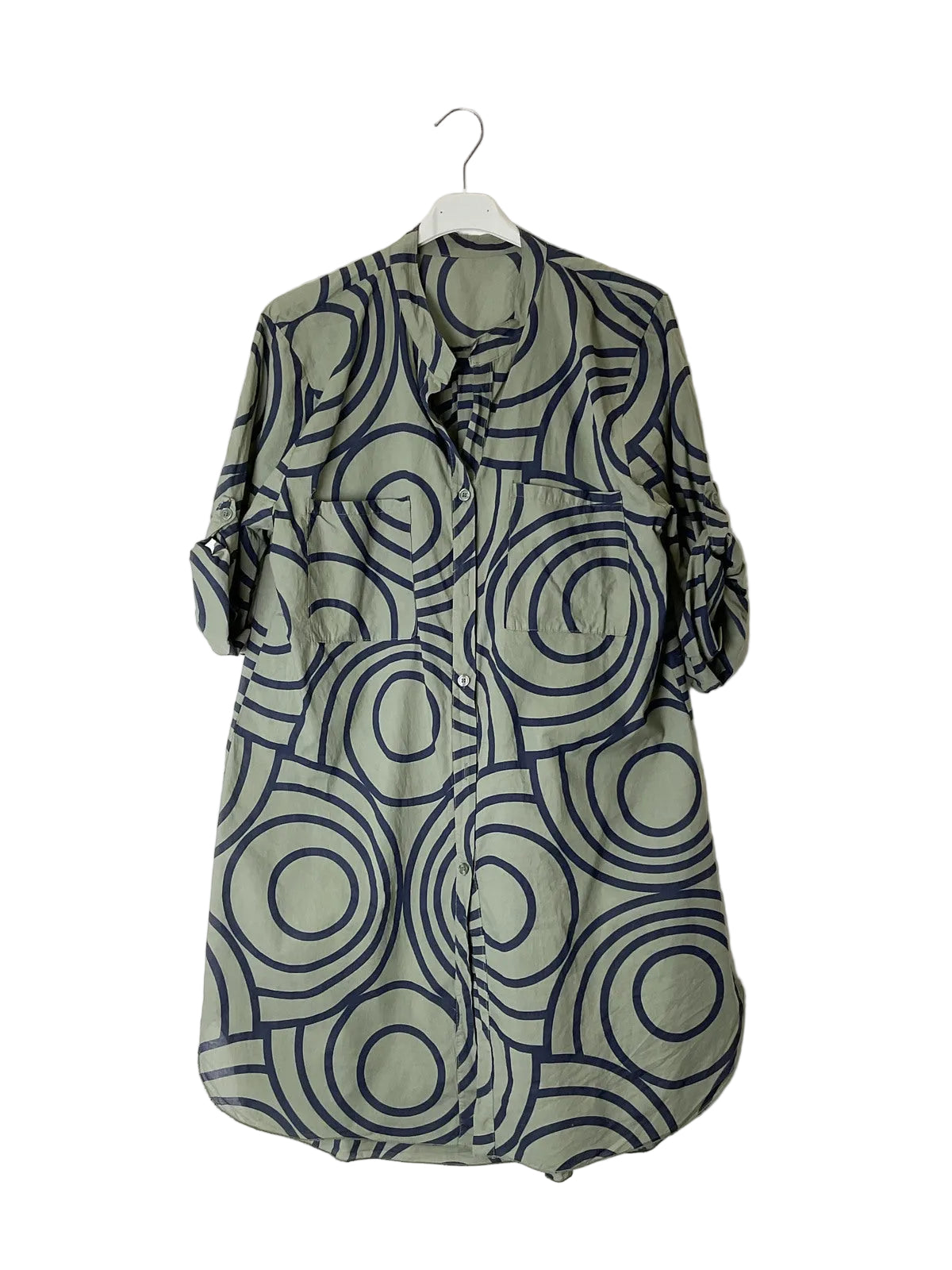 An olive green button-up shirt dress with abstract circular pattern, hanging on a white plastic hanger against a plain white wall.