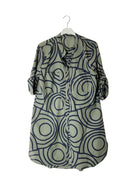 An olive green button-up shirt dress with abstract circular pattern, hanging on a white plastic hanger against a plain white wall.