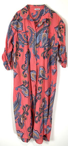 A coral pink long-sleeve button-up shirt dress with a blue, purple, and gold paisley pattern, shown hanging against a plain white background.