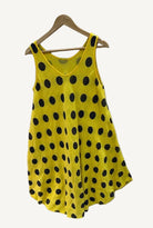 Yellow sleeveless dress with black polka dots on a hanger against a white background