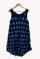 Navy blue sleeveless dress with white polka dots on a hanger against a white background