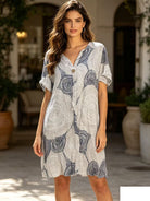 Woman wearing a patterned dress standing outdoors with plants and furniture in the background