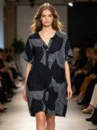 Model wearing a black dress with white patterns on a runway