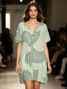 Model wearing a green patterned dress on a runway with an audience.