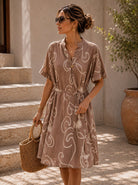 Woman in a patterned dress holding a woven bag outdoors.