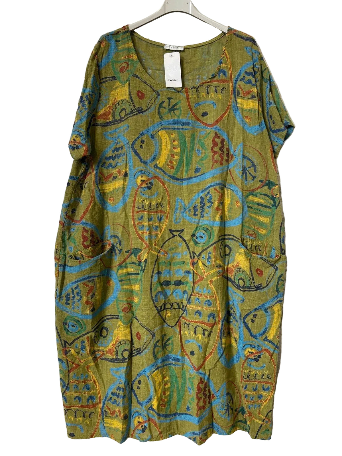 A short-sleeve tunic dress with an abstract fish pattern in olive green, yellow, blue, and red, hanging on a hanger against a textured gray background.