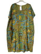 A short-sleeve tunic dress with an abstract fish pattern in olive green, yellow, blue, and red, hanging on a hanger against a textured gray background.