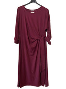 A long-sleeve, crew-neck dress in deep burgundy. The dress features a gathered twist detail at the waist and a side tie.