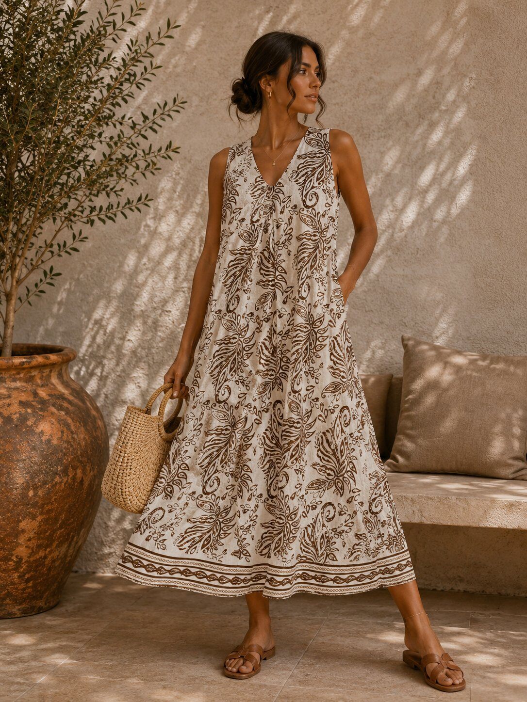 Woman in a patterned dress standing in a sunlit room with a plant and sofa.