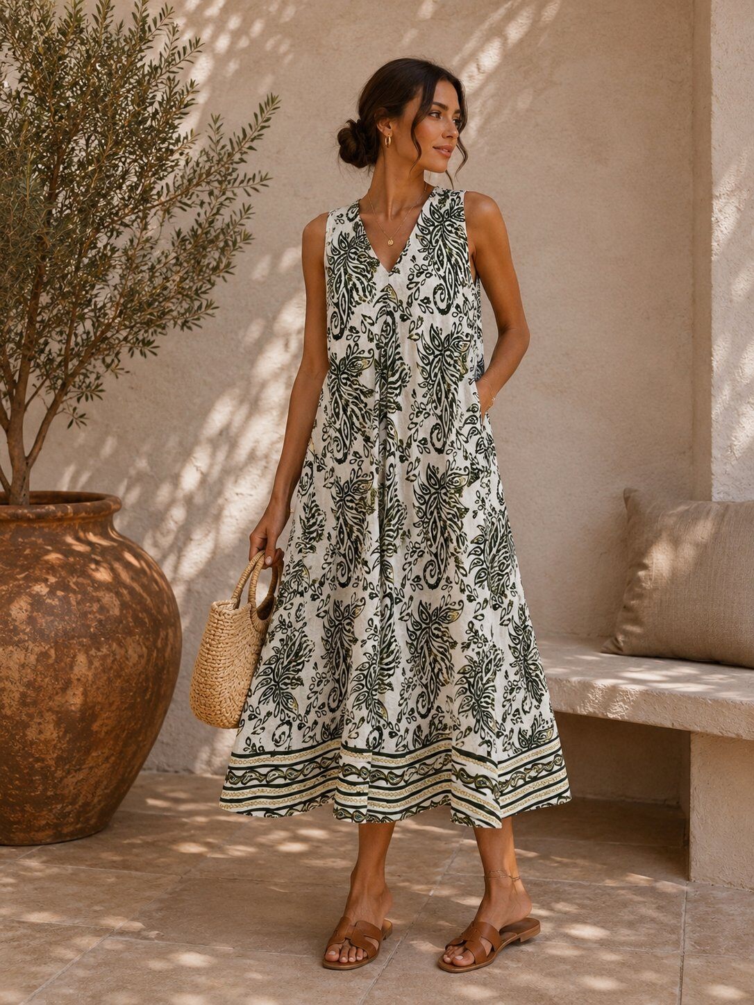 Woman wearing a white dress with olive green patterns standing outdoors near a large vase and bench.