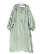 A light sage green textured dress with balloon sleeves and a split neckline, hanging on a white hanger