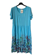 A short-sleeve A-line dress in bright turquoise blue, featuring a floral print concentrated along the bottom hem. 
