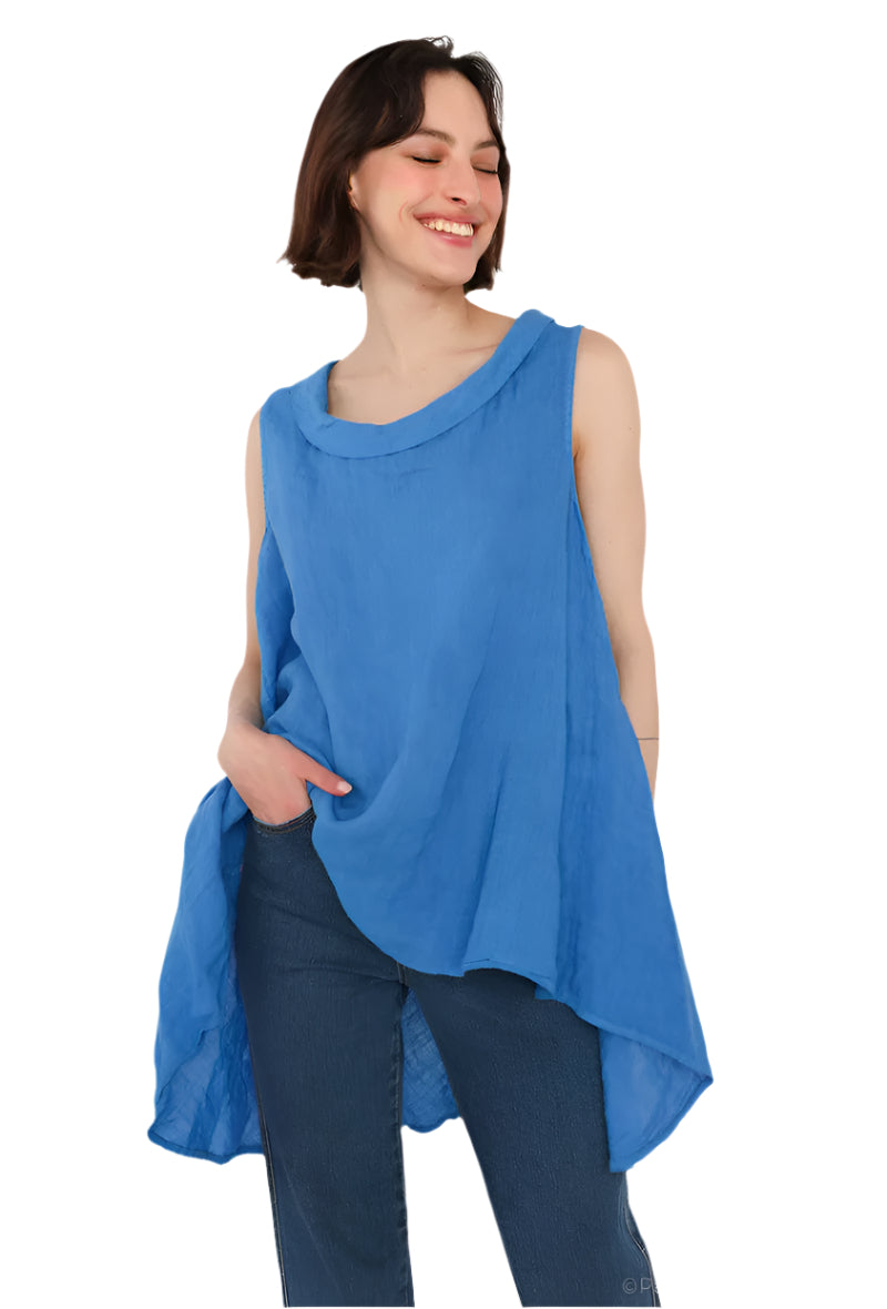 A woman wearing a royal blue sleeveless cowl neck top with an asymmetrical hem, paired with white trousers.