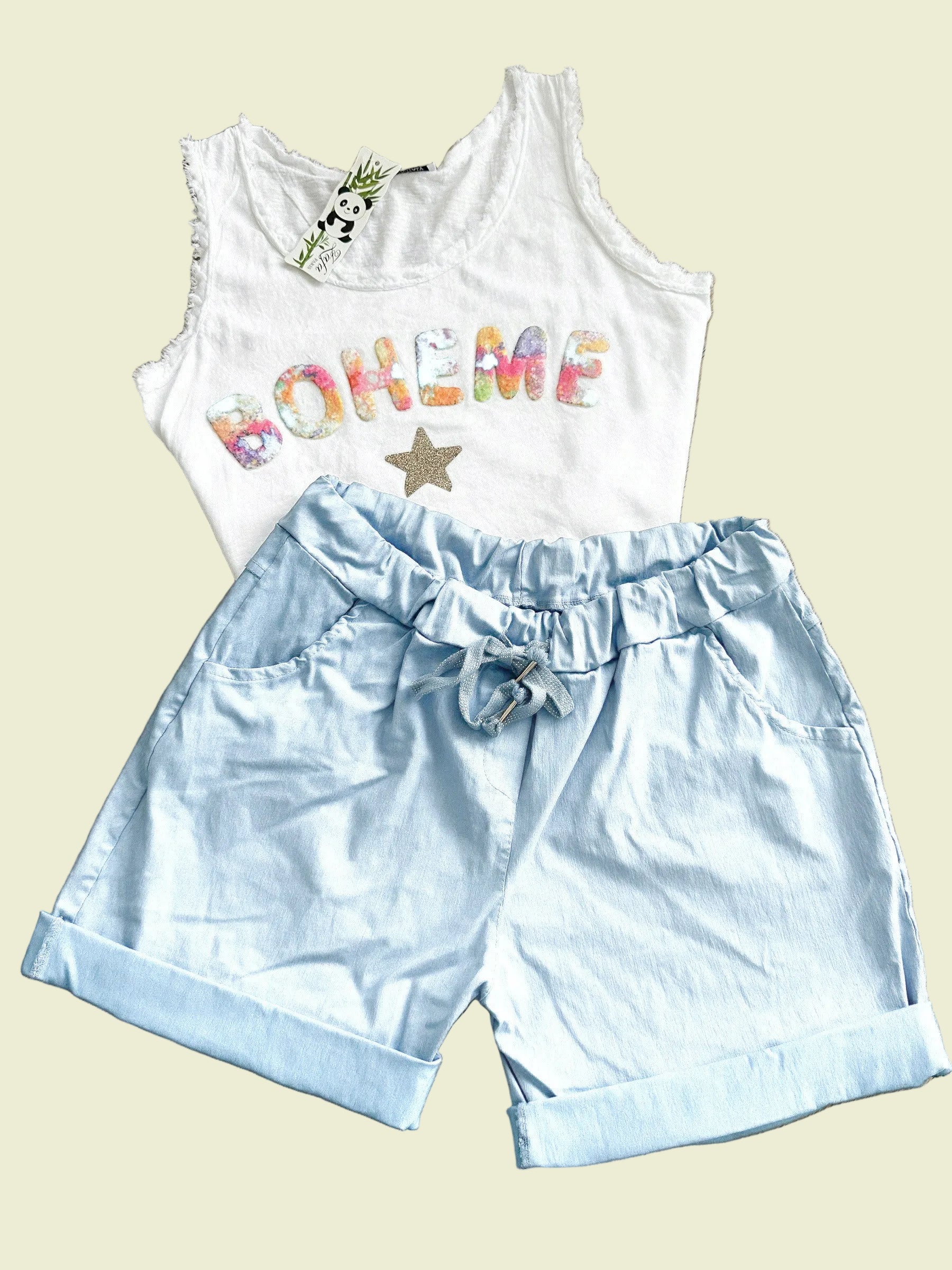 White sleeveless top with colorful text and light blue shorts on a wooden floor