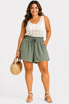 Woman wearing a white lace top and green shorts with a straw bag on a white background