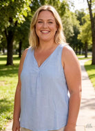 Woman in a light blue sleeveless top standing outdoors with greenery in the background
