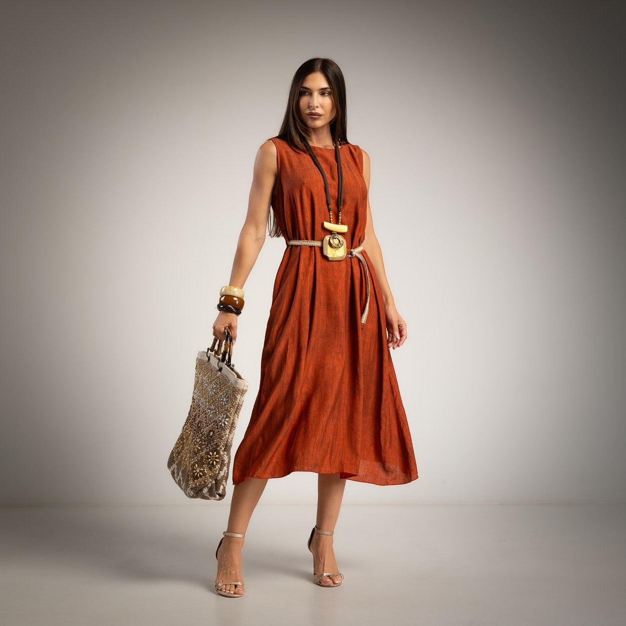 A woman models a sleeveless orange midi dress with a belt 